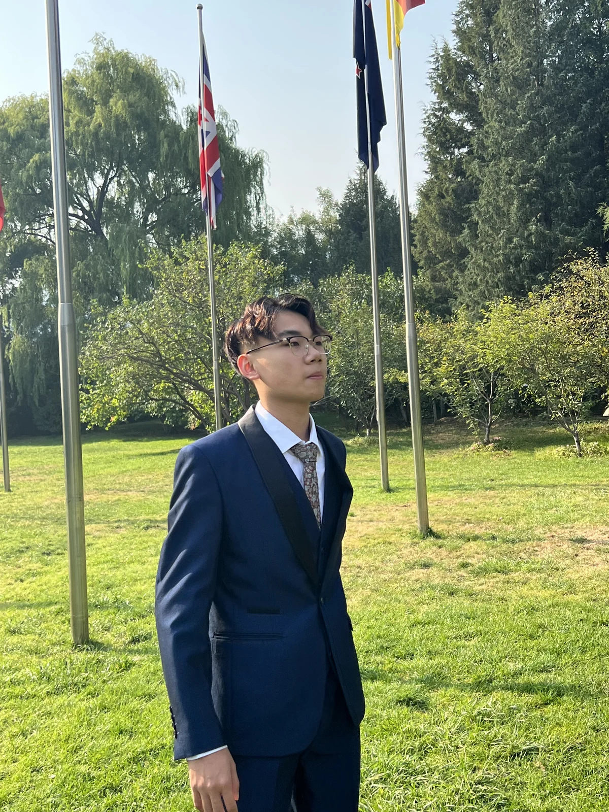 Kaize Zheng wearing a navy suit outdoors near a row of international flags